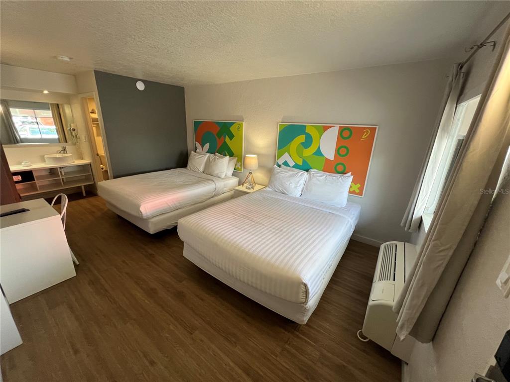 A hotel room features two beds, wood-look flooring, a vanity area, and colorful wall art — 5367 W IRLO BRONSON MEMORIAL HWY UNIT 1-103, KISSIMMEE, FL