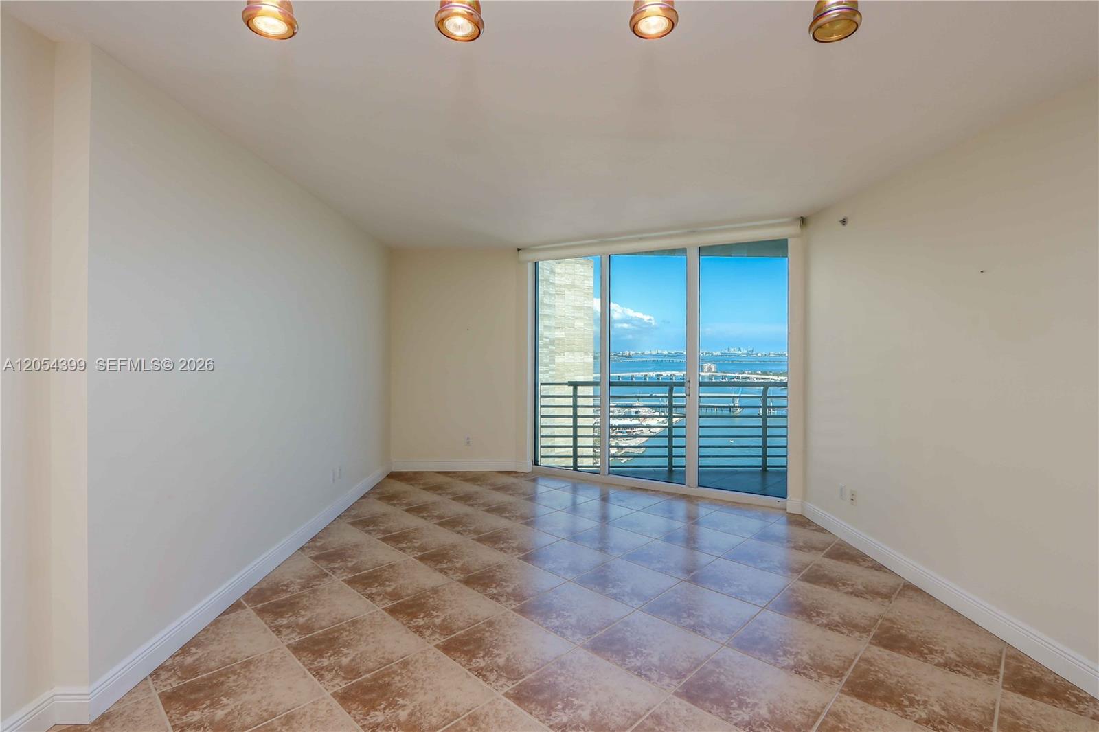 An empty room features beige tile flooring, recessed lighting, and a balcony with water views — 335 S Biscayne Blvd # 3510, Miami FL 33131, MIAMI, FL