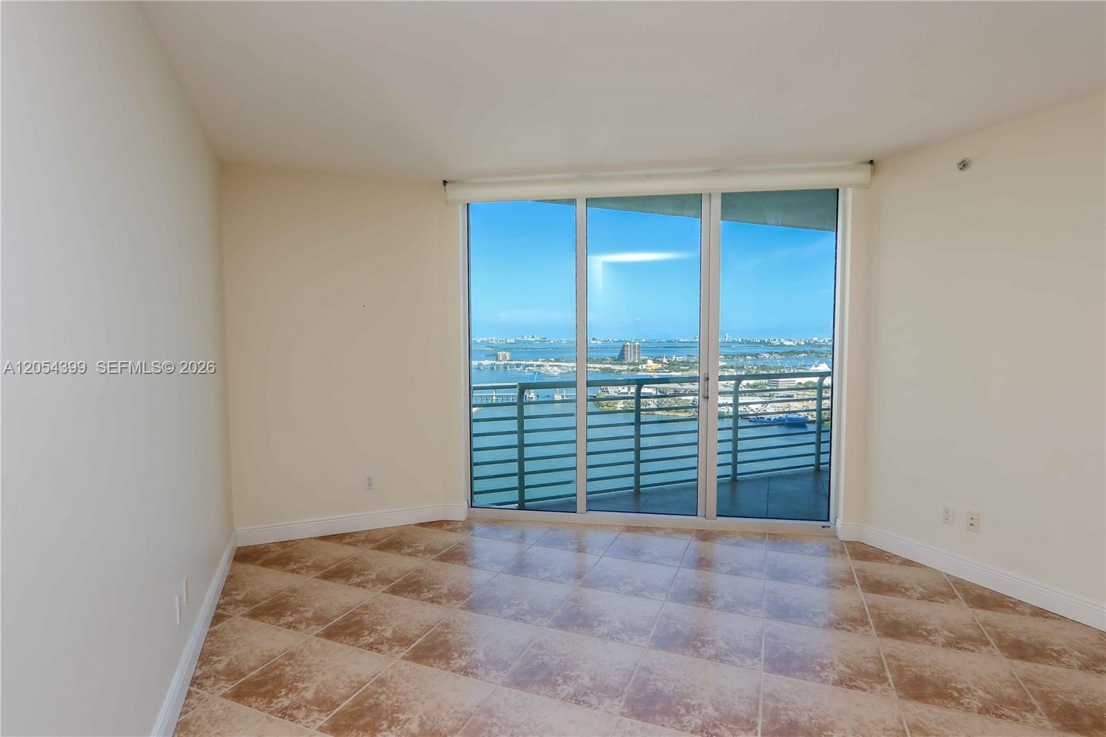 An empty room features beige tile flooring, plain walls, and a large balcony overlooking water — 335 S Biscayne Blvd # 3510, Miami FL 33131, MIAMI, FL