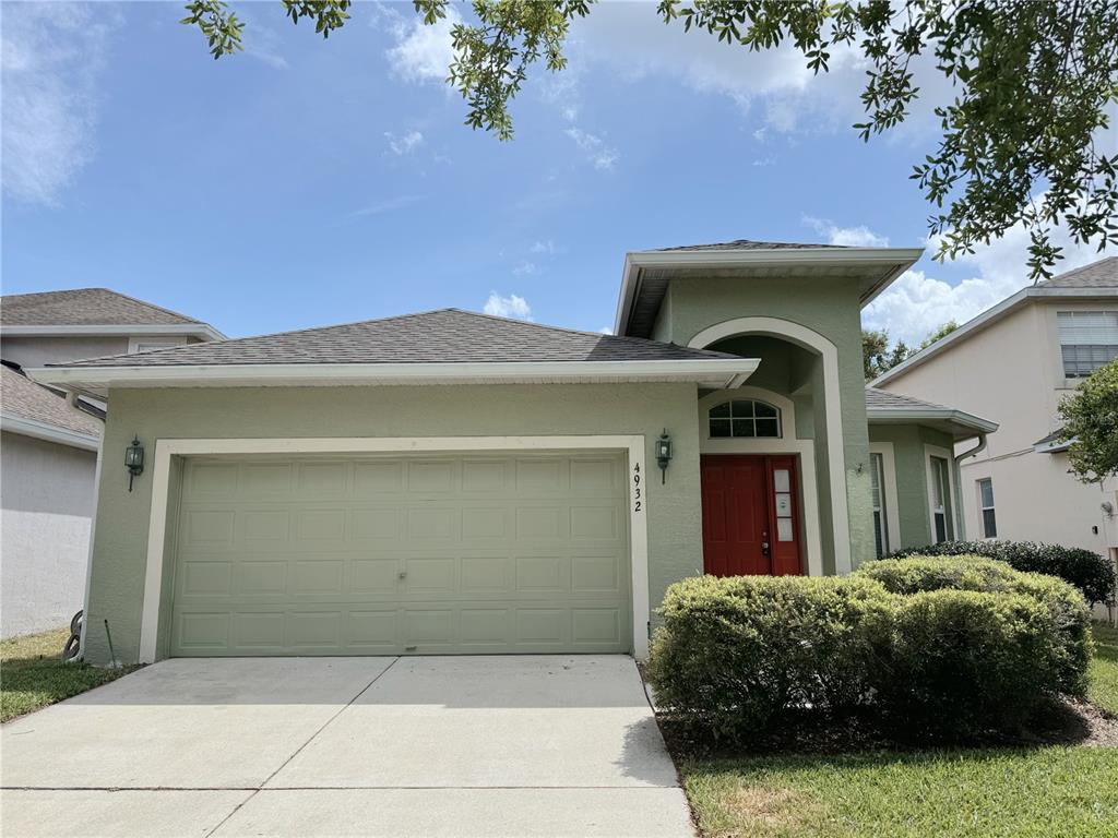 A light green house with a two-car garage and a red front door — 4932 BELLTHORN DRIVE, ORLANDO, FL