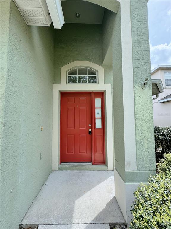A red front door with a side window is set within a green stucco entryway — 4932 BELLTHORN DRIVE, ORLANDO, FL