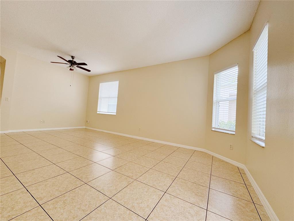 An empty room with beige tile flooring, light walls, a ceiling fan, and three windows — 4932 BELLTHORN DRIVE, ORLANDO, FL