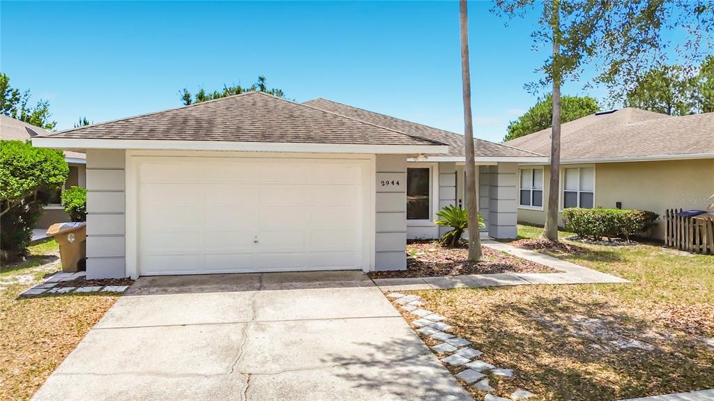 A single-story house features a white garage door, gray siding accents, and a concrete driveway — 2944 SUNSET VISTA BOULEVARD, KISSIMMEE, FL