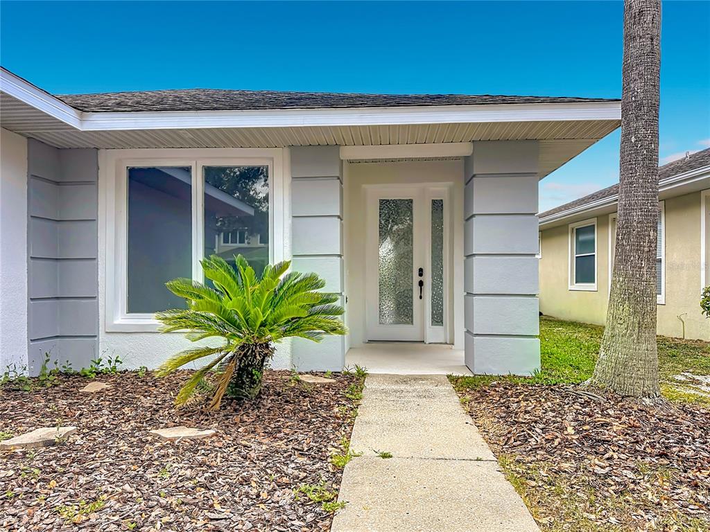 A front view of a house exterior featuring a white door, gray columns, and landscaping — 2944 SUNSET VISTA BOULEVARD, KISSIMMEE, FL