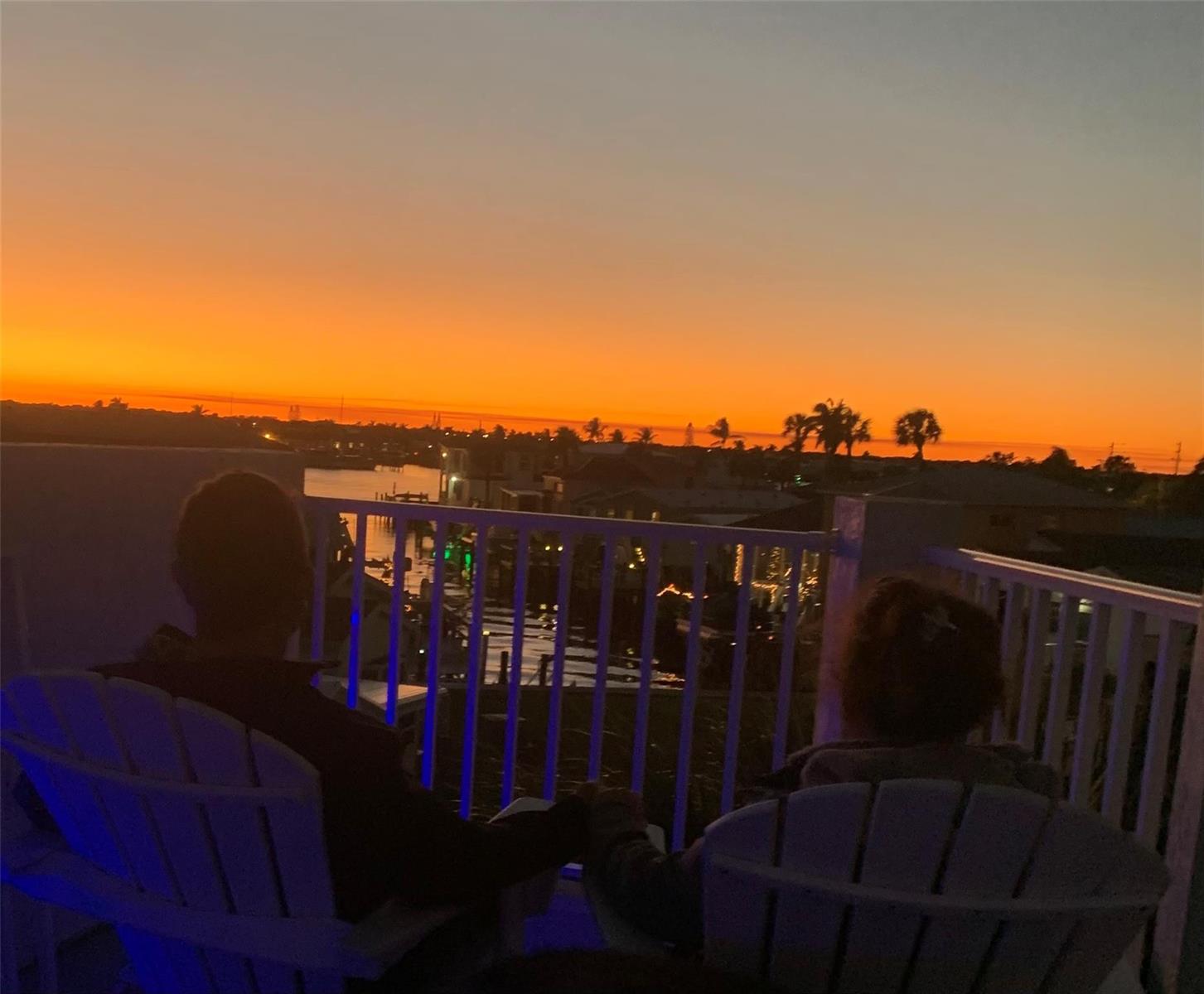 Two people sit on a balcony overlooking a canal at sunset — 2045 Nettles Boulevard, Jensen Beach FL 34957, JENSEN BEACH, FL