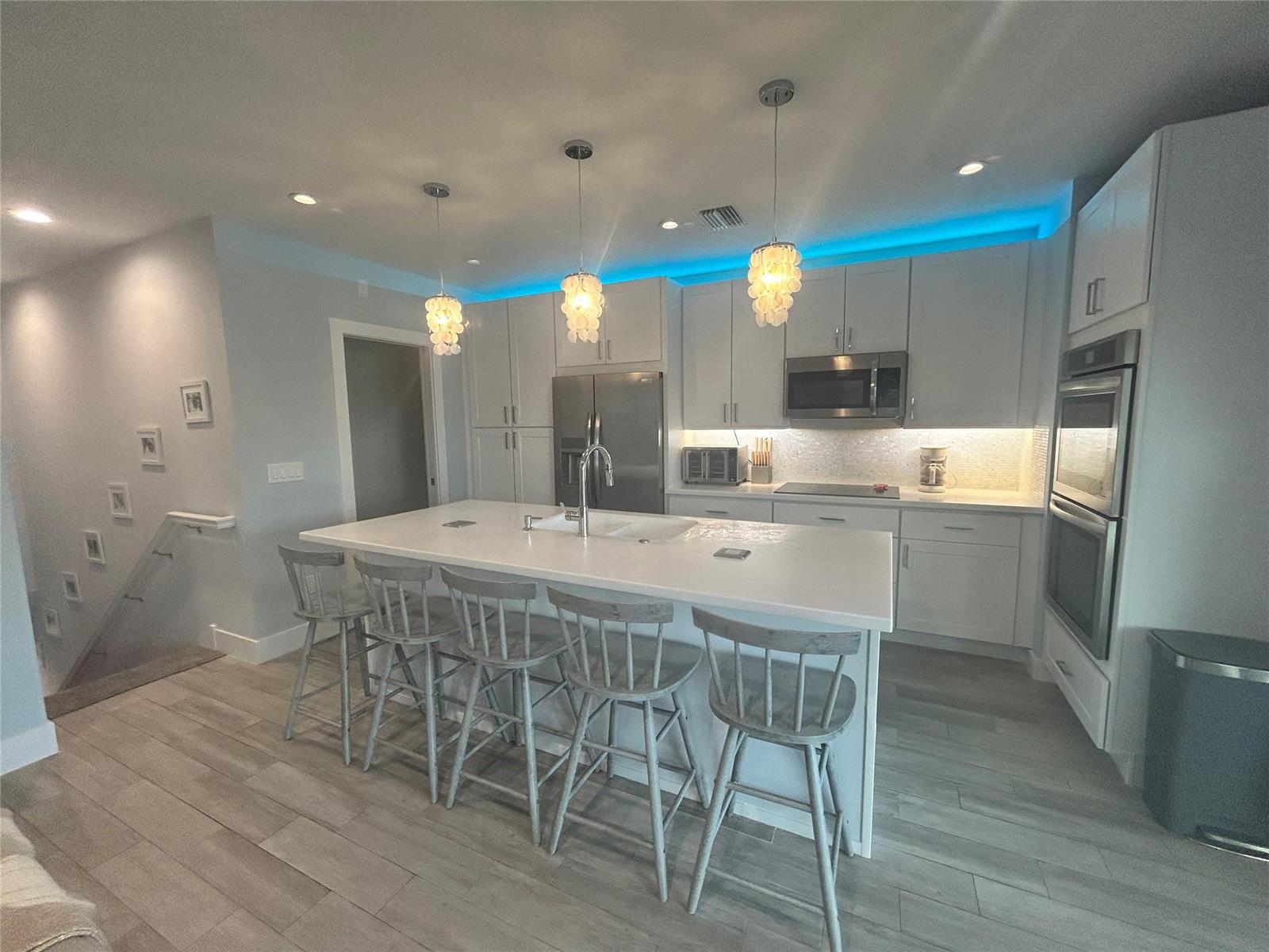 A modern kitchen features white cabinetry, a large island with bar seating, and blue lighting — 2045 Nettles Boulevard, Jensen Beach FL 34957, JENSEN BEACH, FL