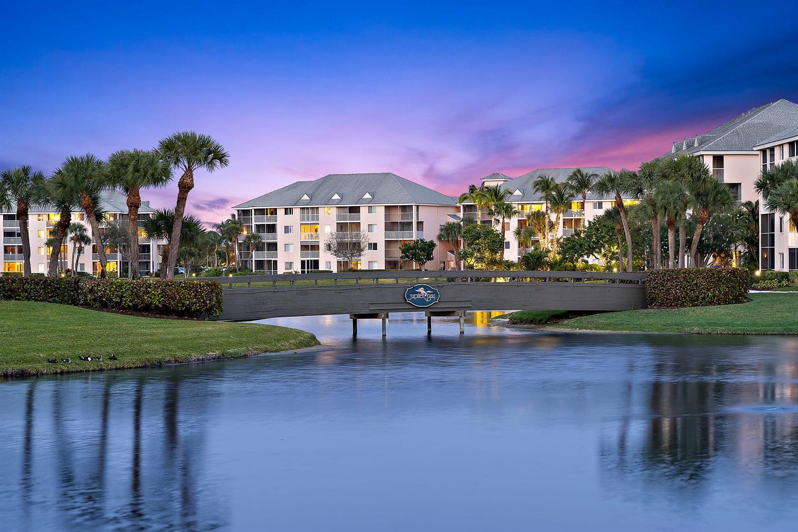 A wooden footbridge spans a pond in front of multi-story apartment buildings at sunset — 353 S Us Highway 1 # A203, Jupiter FL 33477, JUPITER, FL