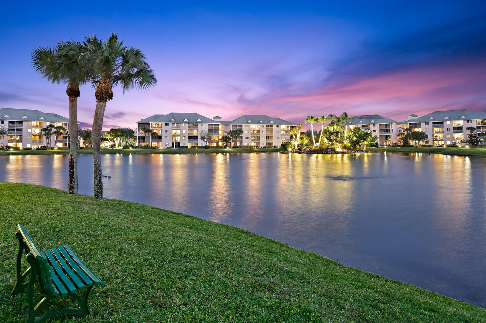 A green bench sits on a grassy lawn overlooking a lake and multi-story apartment buildings — 353 S Us Highway 1 # A203, Jupiter FL 33477, JUPITER, FL