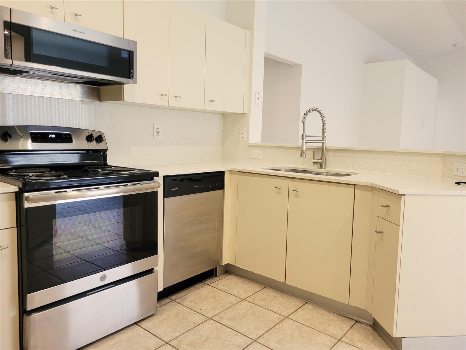 A kitchen features light-colored cabinets, stainless steel appliances, a double sink, and tiled flooring — 1409 Sabal Trail, Weston FL 33327, WESTON, FL