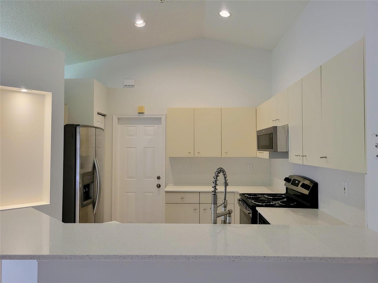 A kitchen features light-colored cabinets, white countertops, stainless steel appliances, and a vaulted ceiling — 1409 Sabal Trail, Weston FL 33327, WESTON, FL