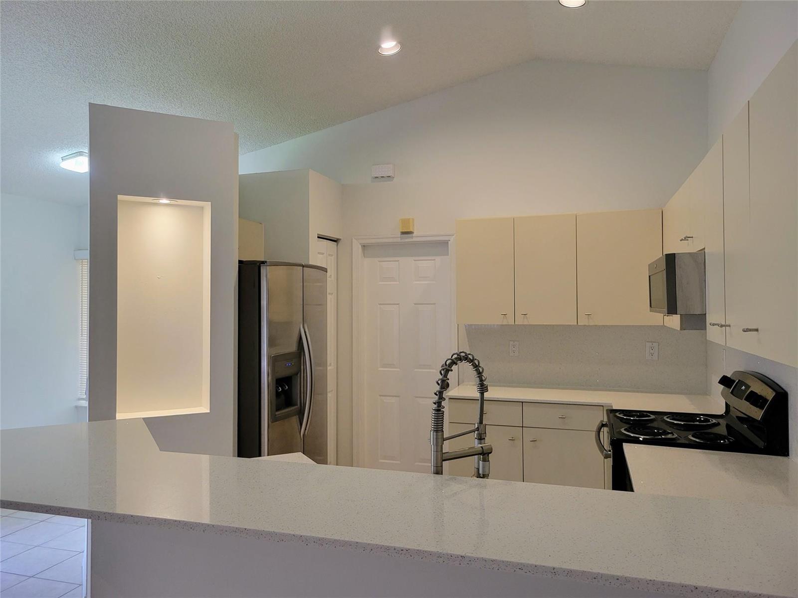 A kitchen features white cabinets, stainless steel appliances, quartz countertops, and a vaulted ceiling — 1409 Sabal Trail, Weston FL 33327, WESTON, FL