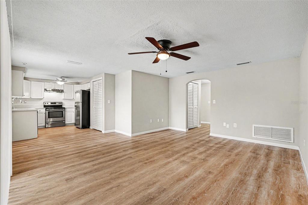 An open-concept living area with light wood-look flooring, a ceiling fan, and an adjacent kitchen — 7030 INGLESIDE DRIVE, PORT RICHEY, FL