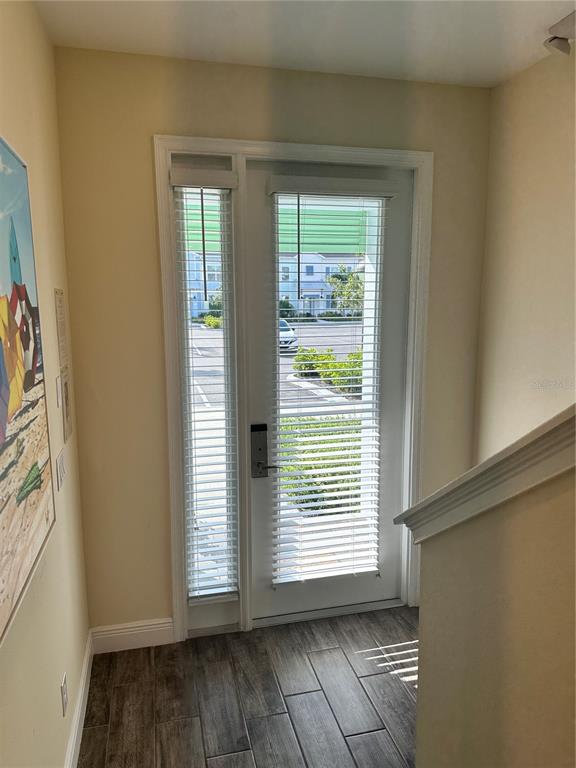 A view of a doorway with white blinds, wood-look tile flooring, and a staircase railing — 2976 ON THE ROCKS POINT, KISSIMMEE, FL