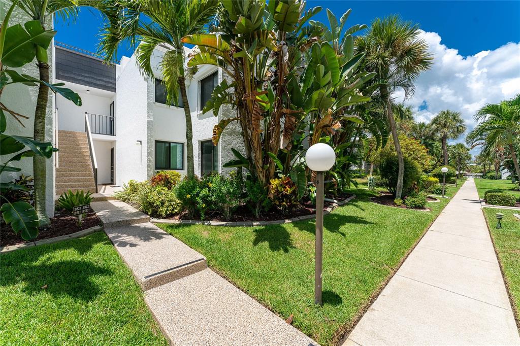A concrete walkway leads to the entrance of a white two-story building with tropical landscaping — 2950 N BEACH ROAD UNIT B522, ENGLEWOOD, FL