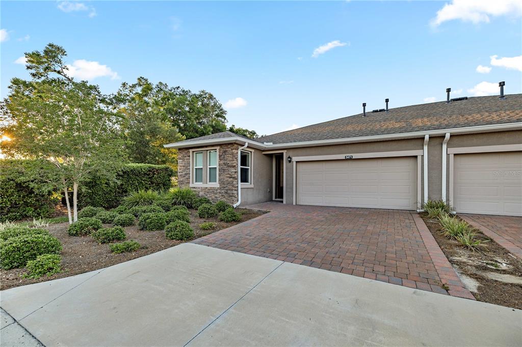 A single-story townhouse with a stone facade, paved driveway, and attached two-car garage — 5471 NW 34TH STREET, OCALA, FL