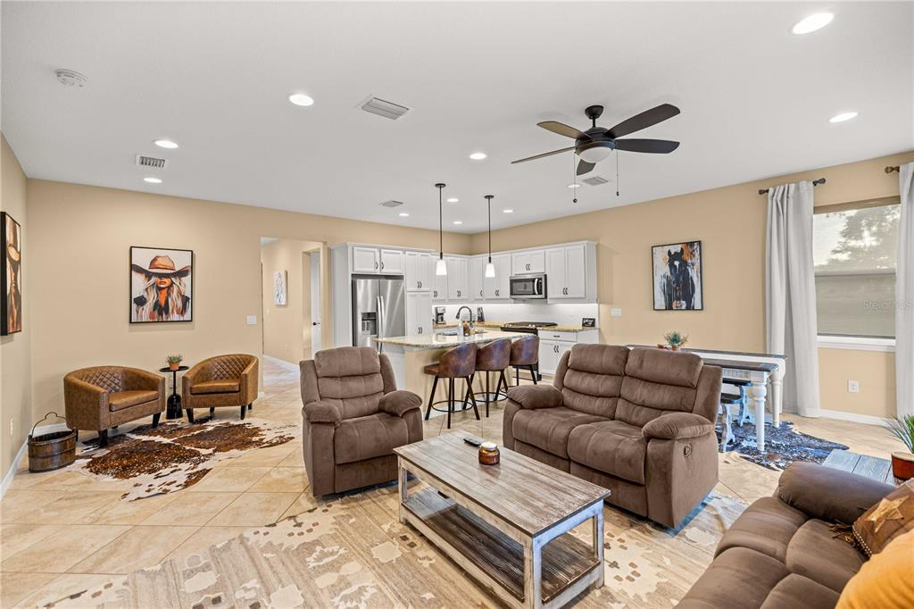 An open-concept living room and kitchen featuring tile flooring, brown furniture, and neutral walls — 5471 NW 34TH STREET, OCALA, FL