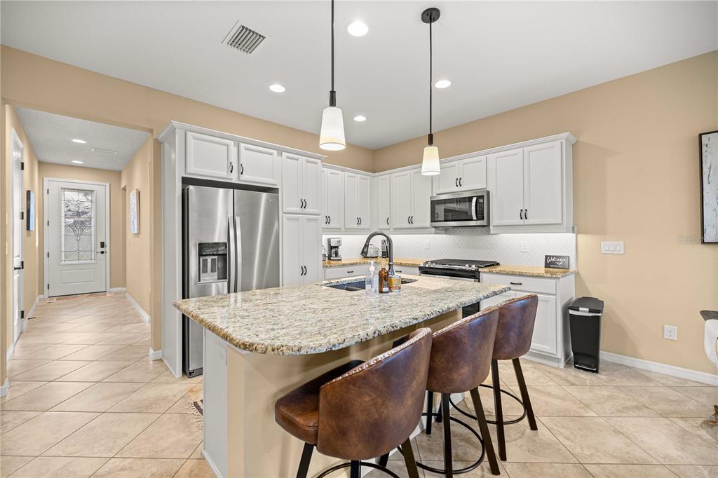 A kitchen with white cabinets, granite countertops, a center island, and three brown bar stools — 5471 NW 34TH STREET, OCALA, FL