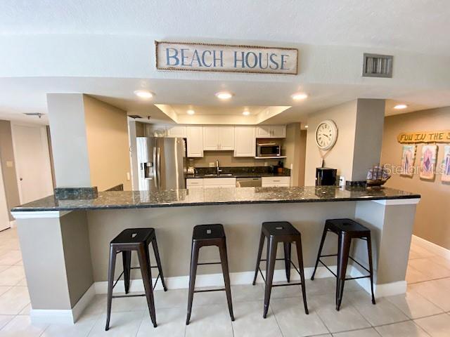 A kitchen features a granite breakfast bar with four metal stools and white cabinetry — 5611 GULF OF MEXICO DRIVE UNIT 5, LONGBOAT KEY, FL