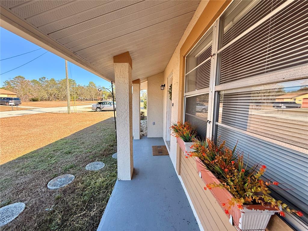 A covered front porch features a concrete floor, stucco columns, and window boxes with artificial plants — 12258 FOOTHILL STREET, SPRING HILL, FL