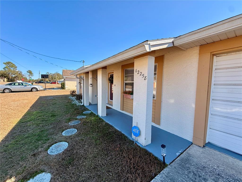 A view of a house exterior featuring a covered porch, a white garage door, and walkway — 12258 FOOTHILL STREET, SPRING HILL, FL