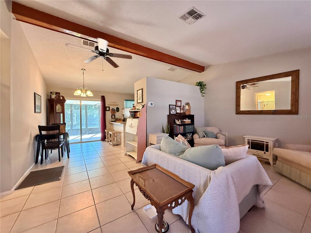 An open-concept living and dining area features tile flooring, a vaulted ceiling, and exposed beams — 12258 FOOTHILL STREET, SPRING HILL, FL