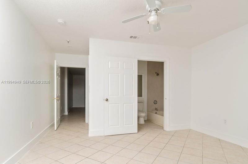 A bedroom with white walls, tiled floors, a ceiling fan, and an attached bathroom — 2734 Bird Ave # 310, Miami FL 33133, MIAMI, FL