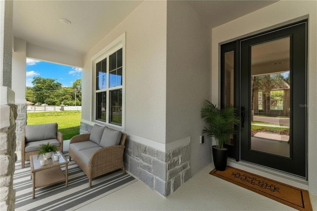 A covered front porch features wicker furniture, a striped rug, and a black glass-paneled door — 2363 HUANIER COURT, APOPKA, FL