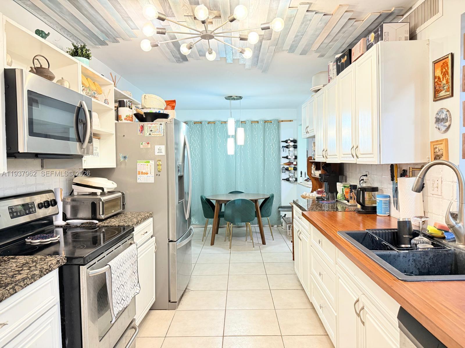 A galley kitchen features white cabinets, wood countertops, stainless steel appliances, and a dining area — 3330 Atlanta St # 14C, Hollywood FL 33021, HOLLYWOOD, FL