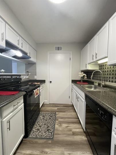 A galley kitchen features white cabinets, dark countertops, black appliances, and wood-look flooring — 2315 N Congress Ave # 21, Boynton Beach FL 33426, BOYNTON BEACH, FL
