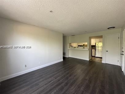 An empty living room with dark wood-look flooring, white walls, and a kitchen pass-through window — 2315 N Congress Ave # 21, Boynton Beach FL 33426, BOYNTON BEACH, FL