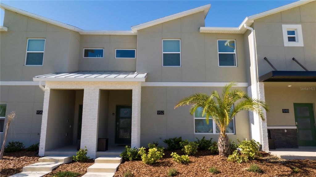 The exterior of a modern two-story townhouse features light-colored siding, brick accents, and a palm tree — 952 LEADER STREET, DAVENPORT, FL