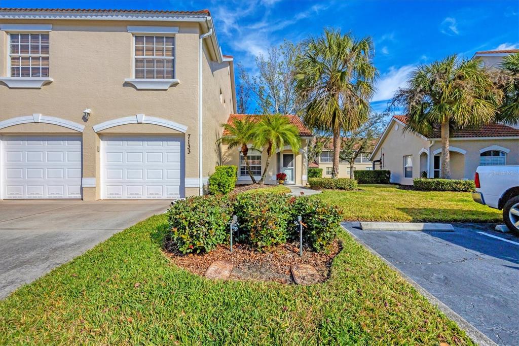 A two-story townhouse exterior features a two-car garage, a small front garden, and palm trees — 7133 CEDAR HOLLOW CIRCLE UNIT 22-102, BRADENTON, FL