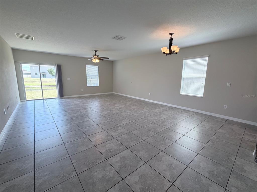 A spacious, empty living room features large gray floor tiles, a ceiling fan, and a chandelier — 10013 CRESTED FRINGE DRIVE, RIVERVIEW, FL