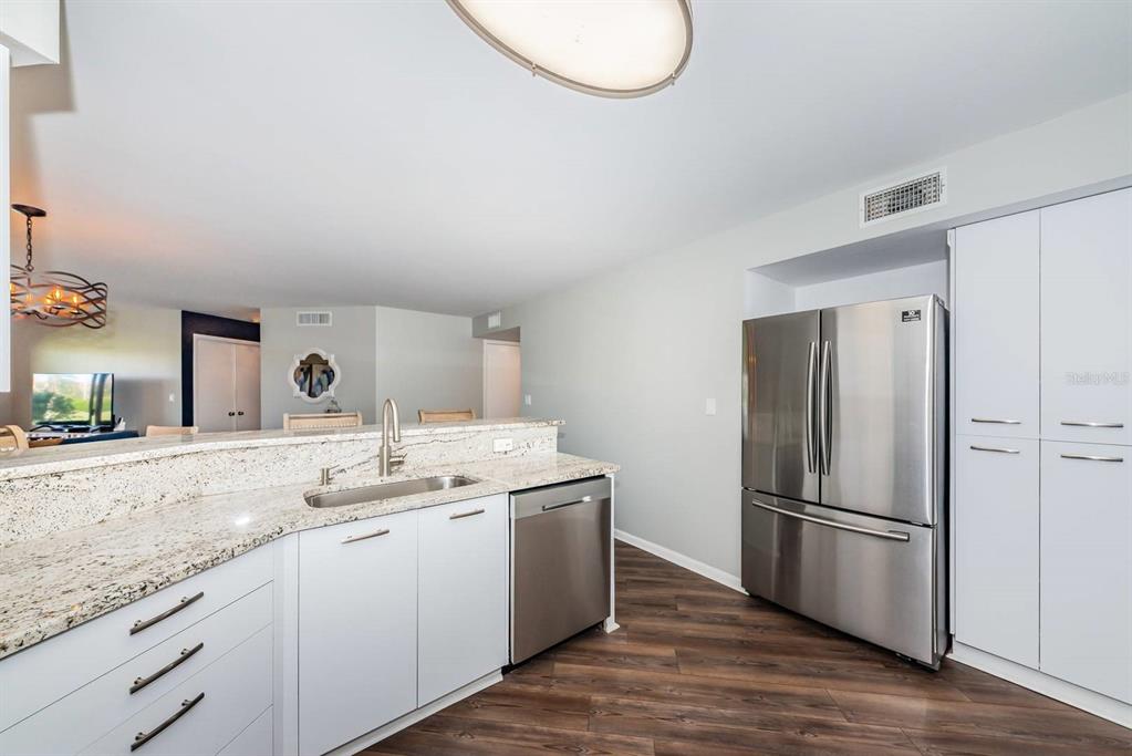 A kitchen features white cabinets, granite countertops, stainless steel appliances, and wood-look flooring — 6151 BAHIA DEL MAR BOULEVARD UNIT 120, ST PETERSBURG, FL