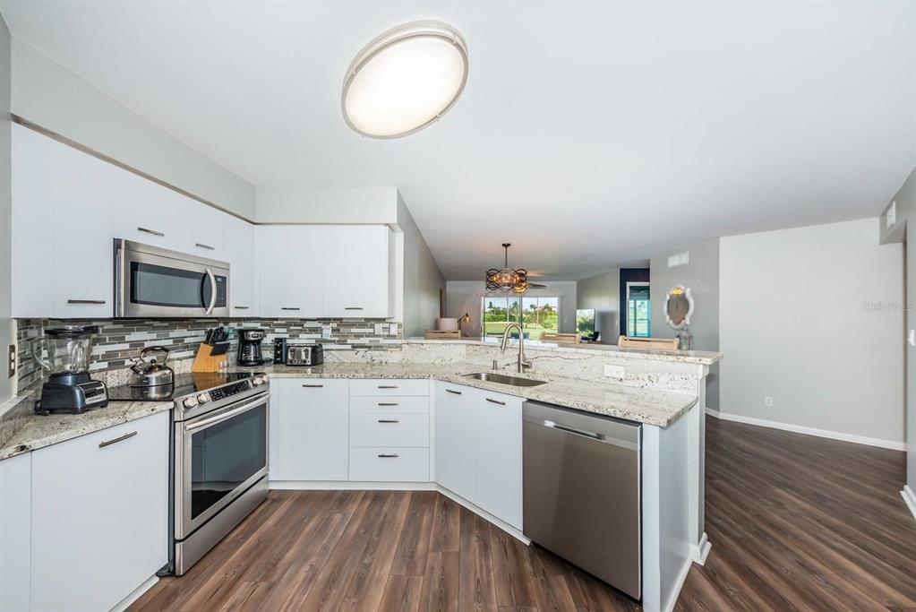 A modern kitchen features white cabinets, stainless steel appliances, granite countertops, and wood-look flooring — 6151 BAHIA DEL MAR BOULEVARD UNIT 120, ST PETERSBURG, FL