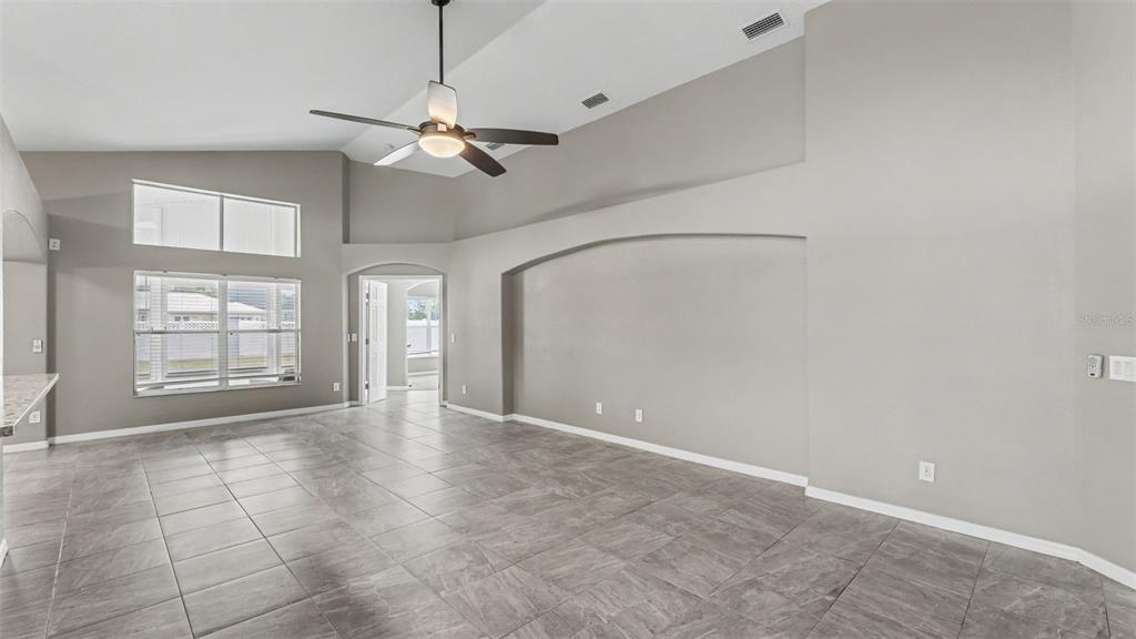 A spacious living room features gray tile flooring, vaulted ceilings, and a large arched wall niche — 8435 ADELE ROAD, LAKELAND, FL