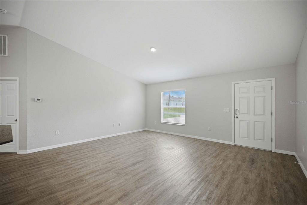 An empty living room with light gray walls, wood-look flooring, a window, and two doors — 2824 SW 161ST LOOP, OCALA, FL