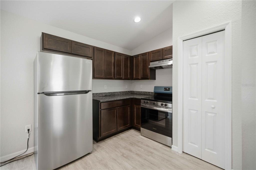 A kitchen features dark wood cabinets, granite countertops, stainless steel appliances, and light wood flooring — 2824 SW 161ST LOOP, OCALA, FL