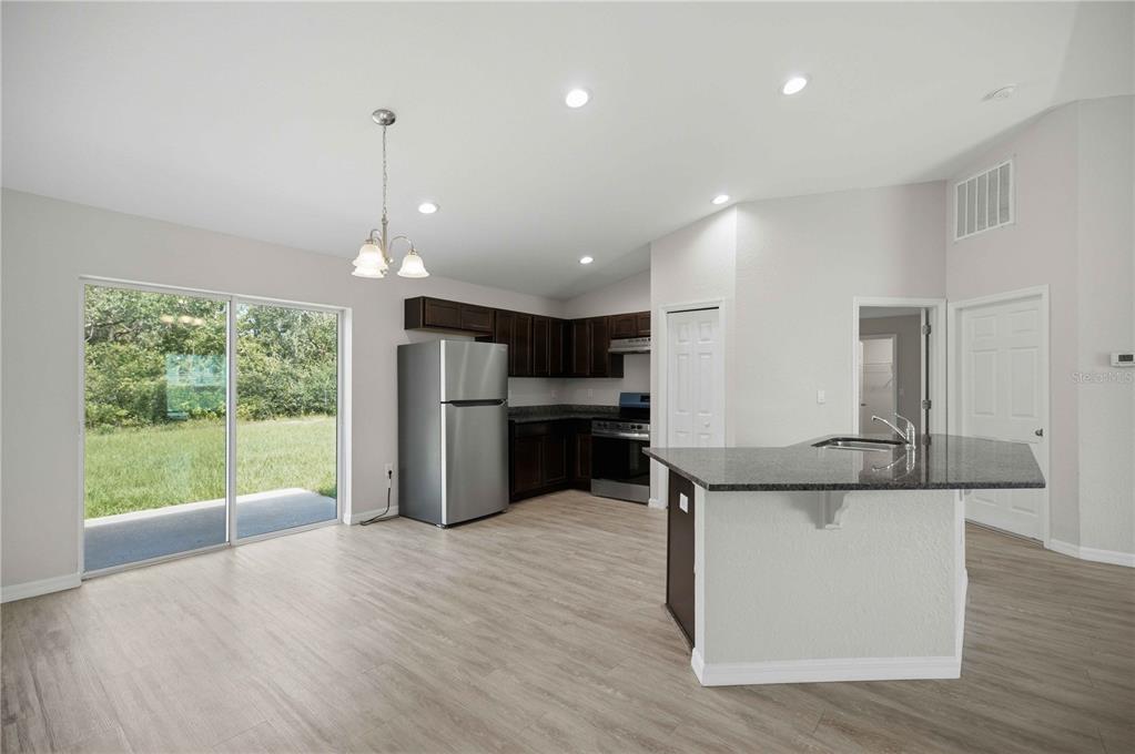 A kitchen with dark cabinets, stainless steel appliances, a granite island, and a sliding glass door — 2824 SW 161ST LOOP, OCALA, FL
