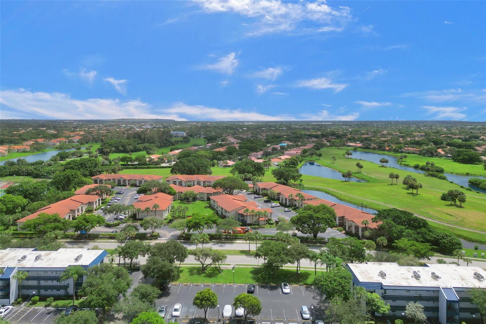 An aerial view shows apartment buildings surrounded by green lawns, ponds, and a parking lot — 3120 Holiday Springs Boulevard # 106, Margate FL 33063, MARGATE, FL