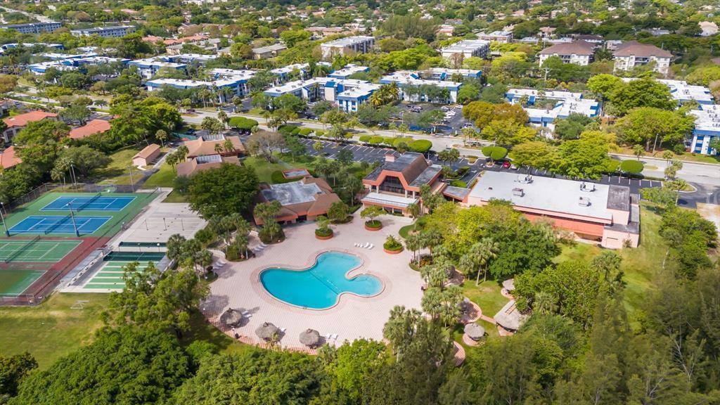 An aerial view shows a swimming pool, tennis courts, and clubhouse surrounded by apartment buildings — 3120 Holiday Springs Boulevard # 106, Margate FL 33063, MARGATE, FL