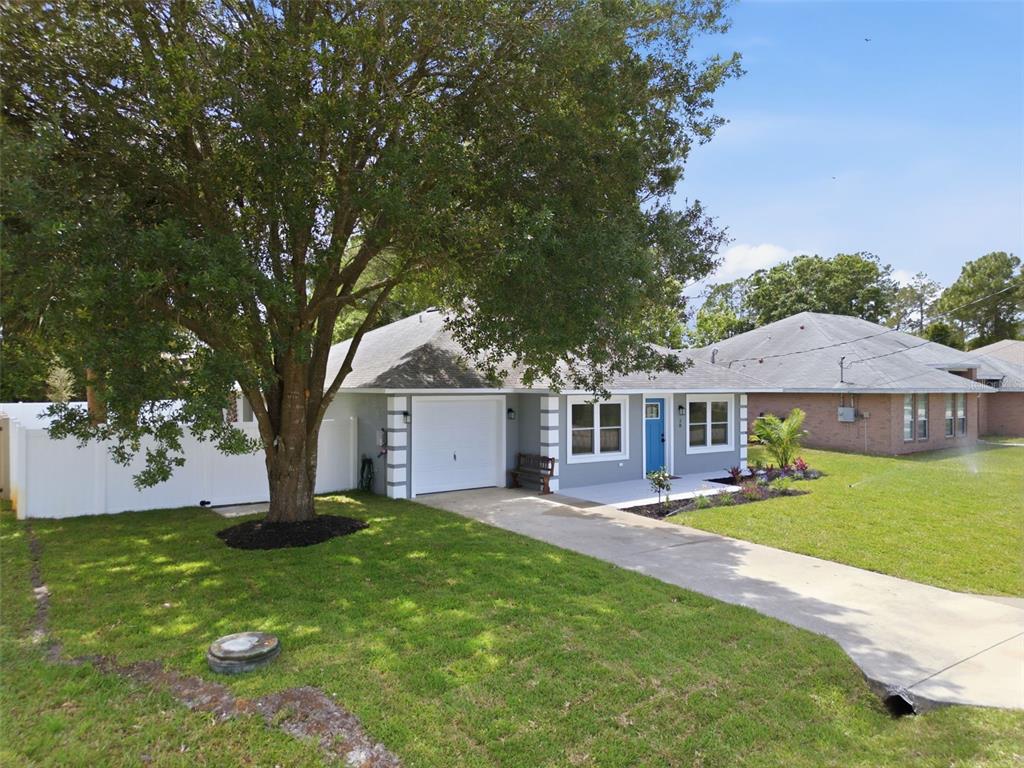 A single-story house with a white garage, blue front door, and a large front tree — 28 PINE CROFT LANE, PALM COAST, FL