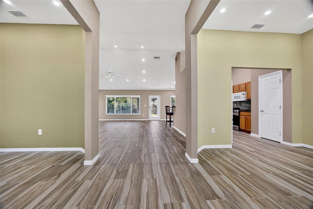 A spacious room with wood-look tile flooring, light green walls, and a view into the kitchen — 25900 AYSEN DRIVE, PUNTA GORDA, FL