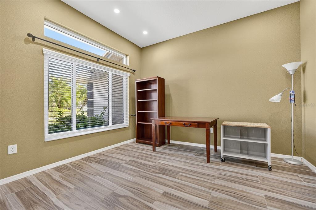 A home office with wood-look tile flooring, a wooden desk, a bookshelf, and a window — 25900 AYSEN DRIVE, PUNTA GORDA, FL
