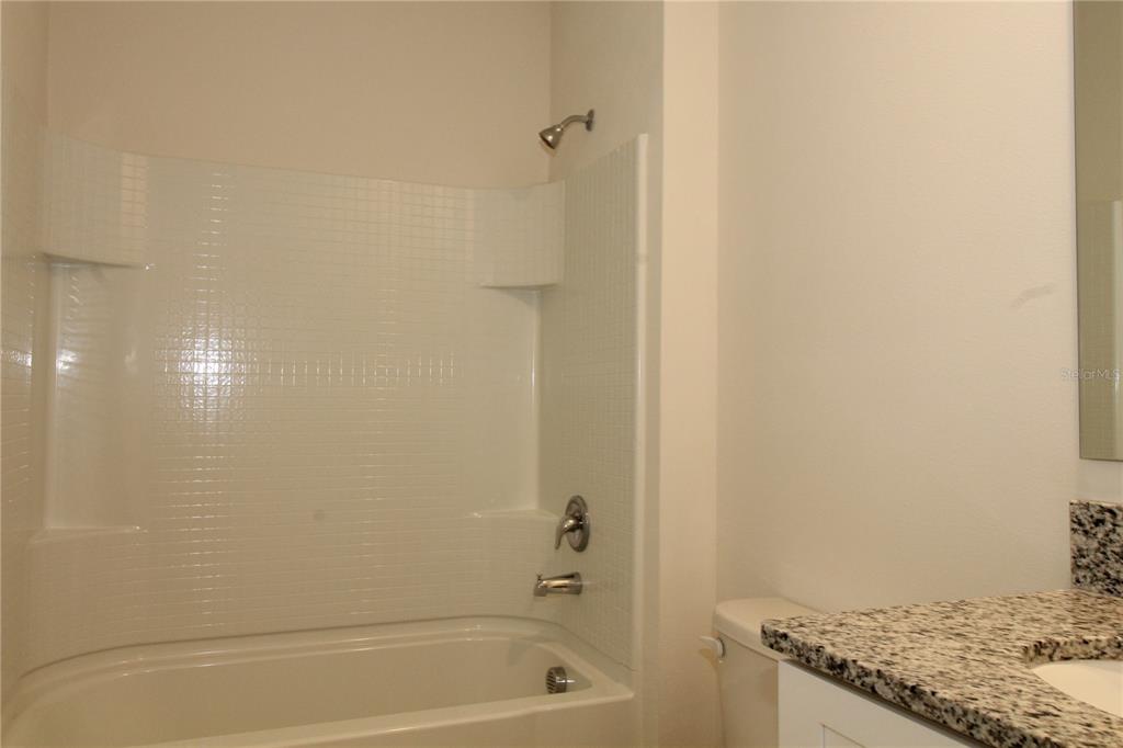 A bathroom features a white tub-shower combination, a granite vanity top, and a toilet — 524 TALISI LOOP, ST CLOUD, FL