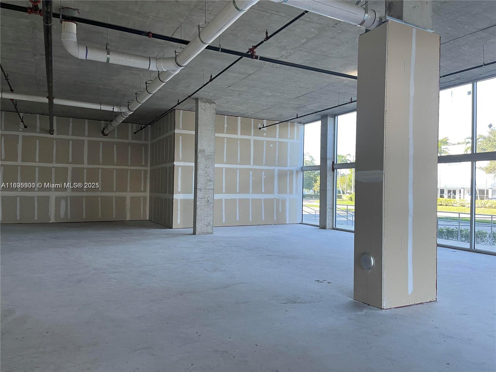 An unfinished commercial interior features exposed concrete ceilings, drywall partitions, and large glass windows — 10450 NW 33rd St # 102, Doral FL 33172, DORAL, FL