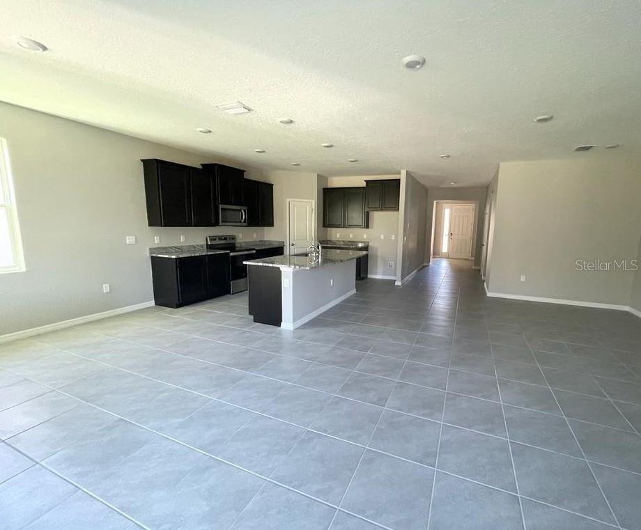 A kitchen with dark cabinets and a granite island opens into a large tiled room — 16988 OVAL RUM DRIVE UNIT 16988, WIMAUMA, FL
