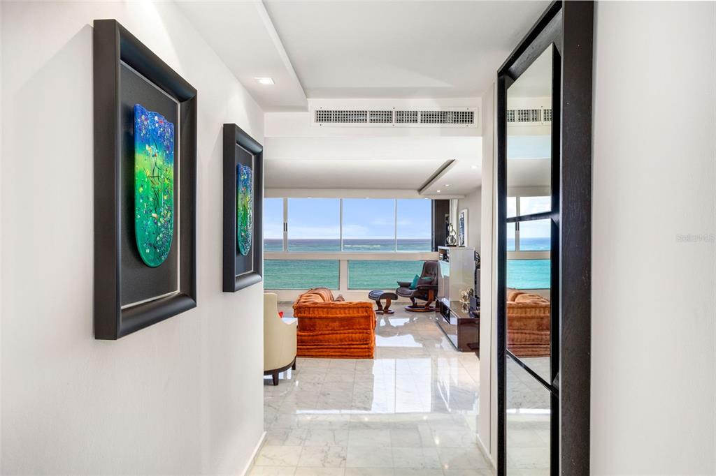 A hallway with framed artwork leads into a living room featuring ocean views and marble floors — Plaza Atlantico AVE ISLA VERDE UNIT 1002, CAROLINA, PR