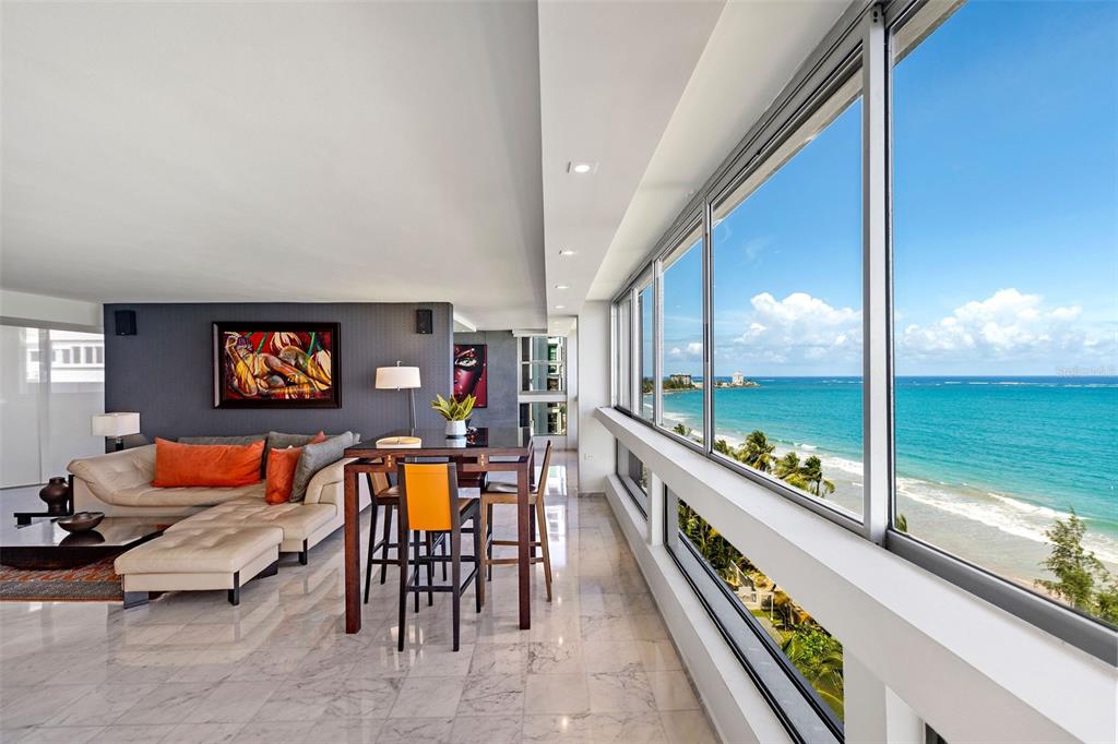 A modern living room with marble floors, a dining set, and floor-to-ceiling ocean view windows — Plaza Atlantico AVE ISLA VERDE UNIT 1002, CAROLINA, PR