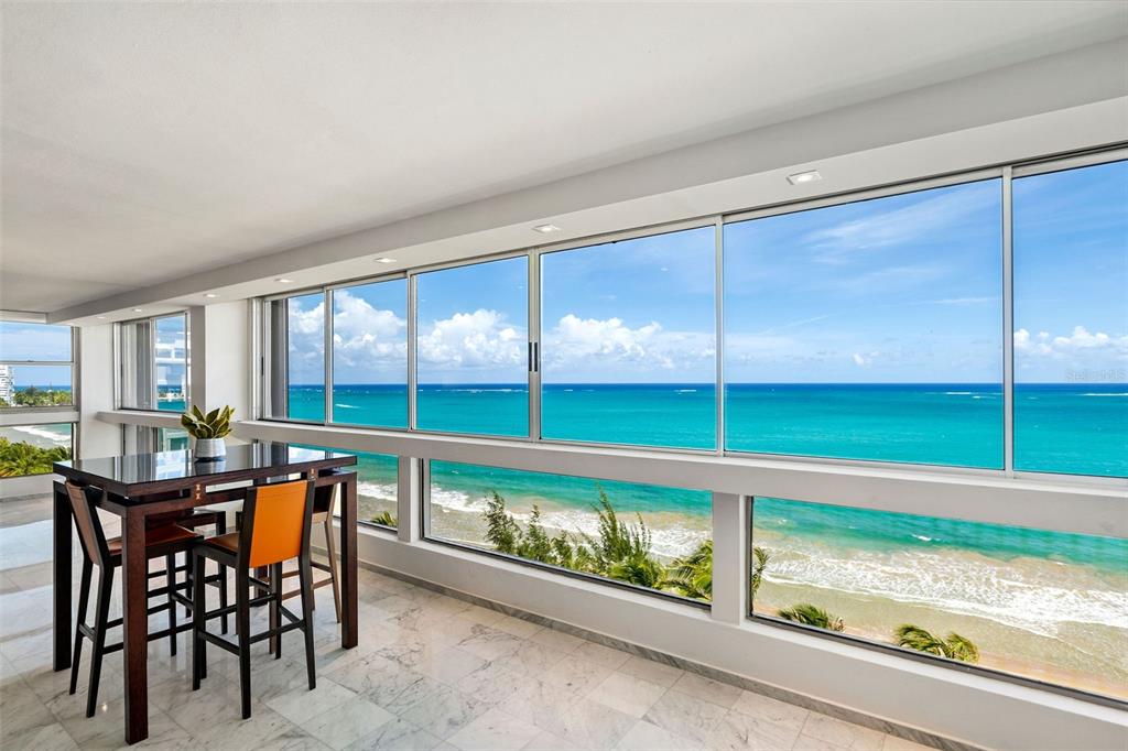 A dining area with a marble floor overlooks the ocean through large floor-to-ceiling windows — Plaza Atlantico AVE ISLA VERDE UNIT 1002, CAROLINA, PR